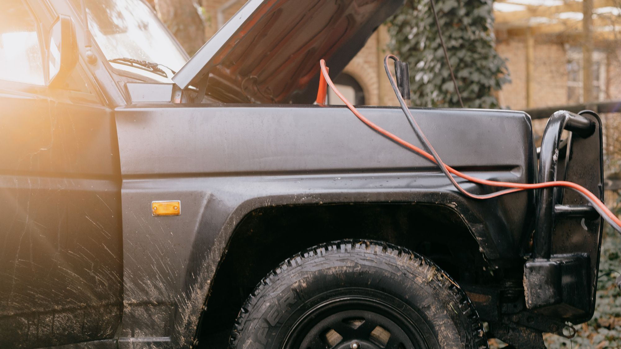 A four wheel drive with the bonnet up and jumper leads connected.