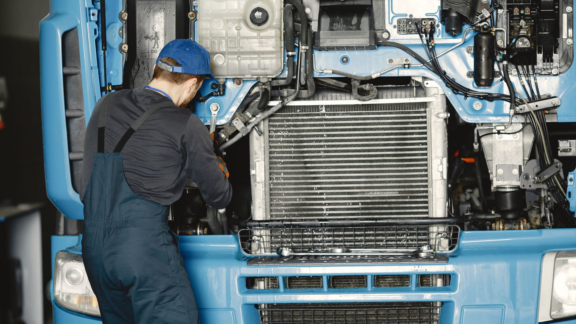 A technician working at the open front of a blue truck cab.