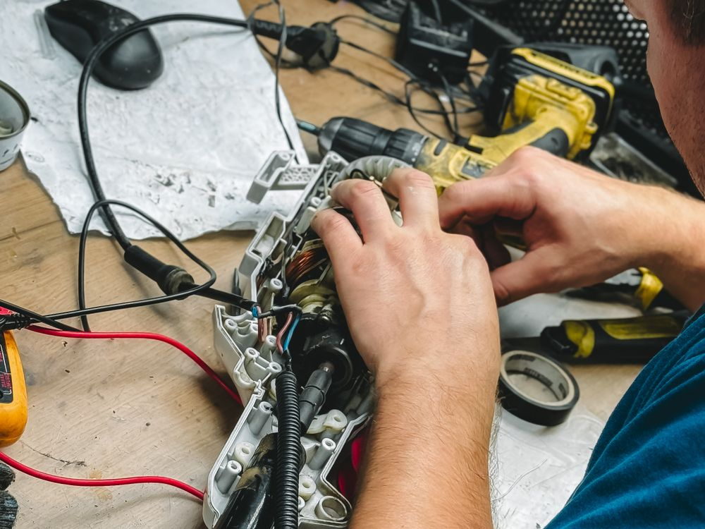 Hands testing a wiring loom with meter probes on a workbench.